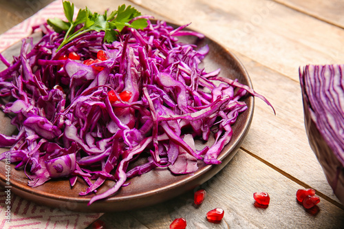 Plate with cut fresh purple cabbage and pomegranate on wooden background, closeup