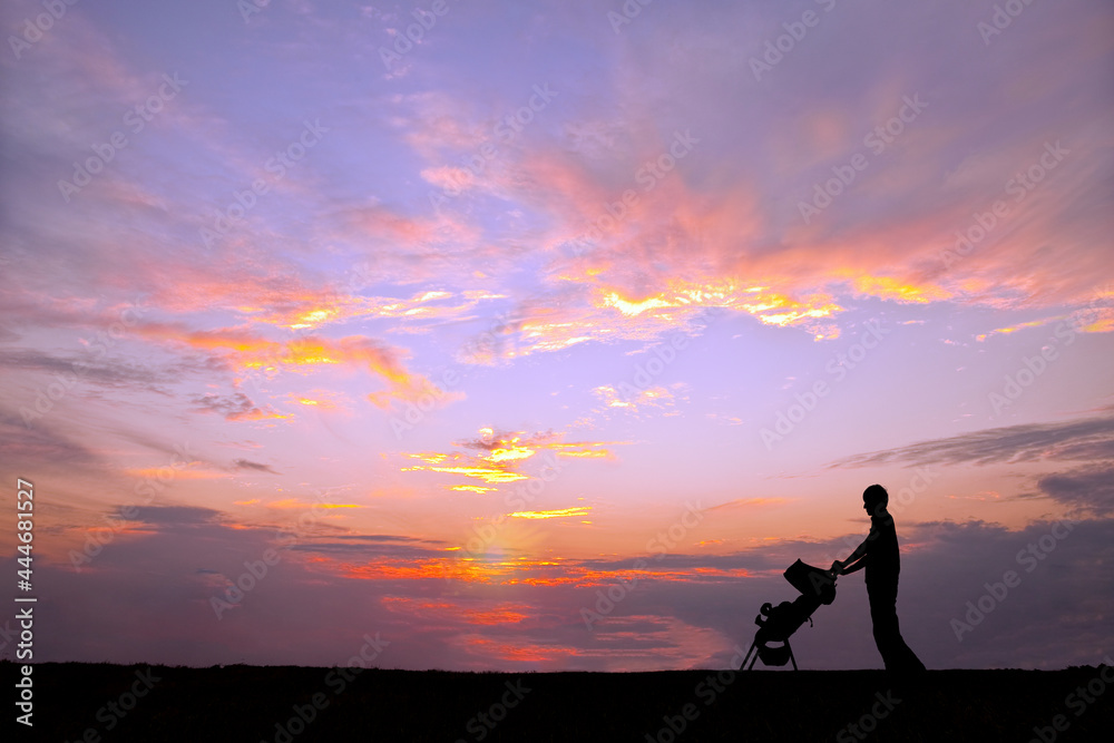 夕日の空を背景にベビーカーを押し散歩をする若い男性