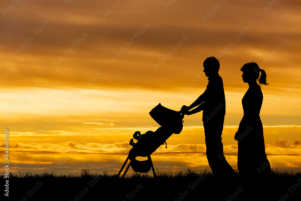 夕日の空を背景にベビーカーを押し散歩をする若い夫婦