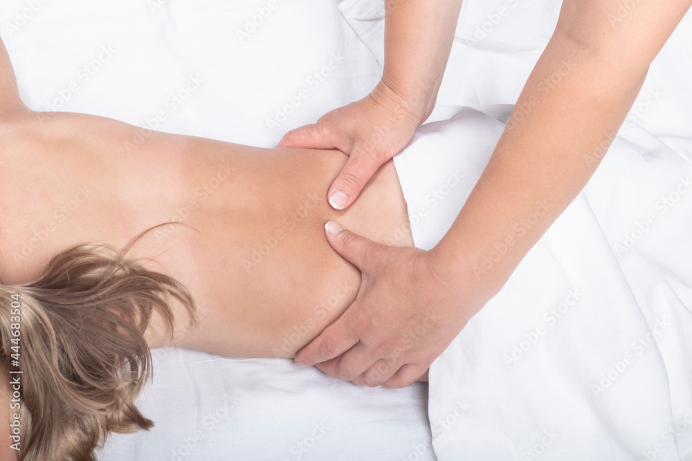 A teenage girl with white hair is lying on her stomach. A professional doctor does a back massage. Close-up. A teenage girl with white hair is lying on her stomach. A professional doctor does a back massage. Close-up.
