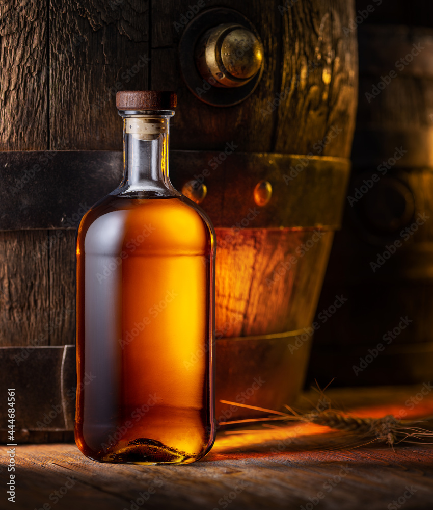 Bottle of whisky and old wooden cask at the background. Bottle of whisky and old wooden cask at the background.