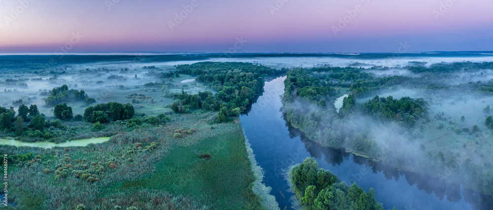 Smoky morning mist over the river. Beautiful panoramic view of river and green banks of the river in the early summer morning.