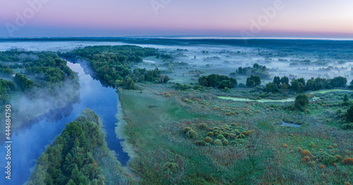 Smoky morning mist over the river. Beautiful panoramic view of river and green banks of the river in the early summer morning. © volff