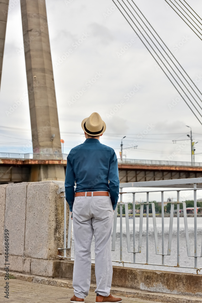 Rear view of thoughtful man, businessman looking at cityscape and river while standing outdoors. Architect looks at the structure of the old bridge and thinks about its renovation.