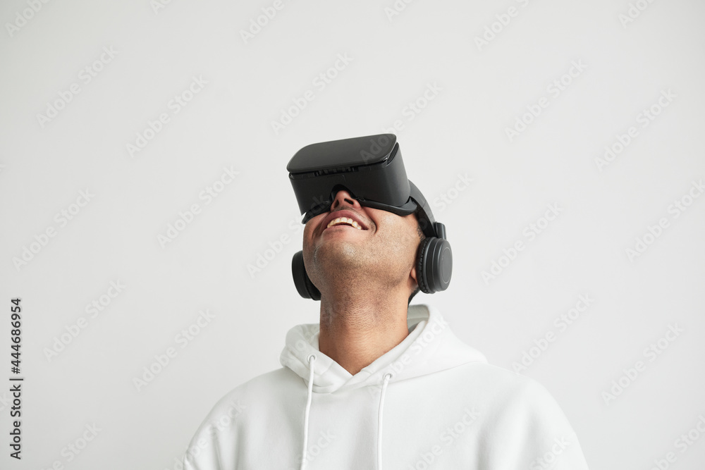 Minimal portrait of modern young man wearing VR headset against white background and looking up, copy space Minimal portrait of modern young man wearing VR headset against white background and looking up, copy space