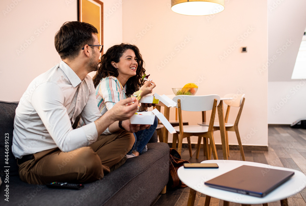 Smiling couple sitting on sofa and eating fast food salad at home. Smiling couple sitting on sofa and eating fast food salad at home.