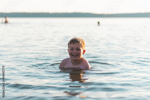 Cute young boy enjoy having fun at lake or river beach water on warm sunset evening time outdoors. © ARVD73