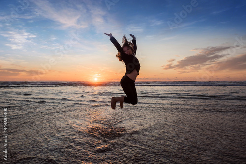 young girl jumping for happiness on the beach at sunset