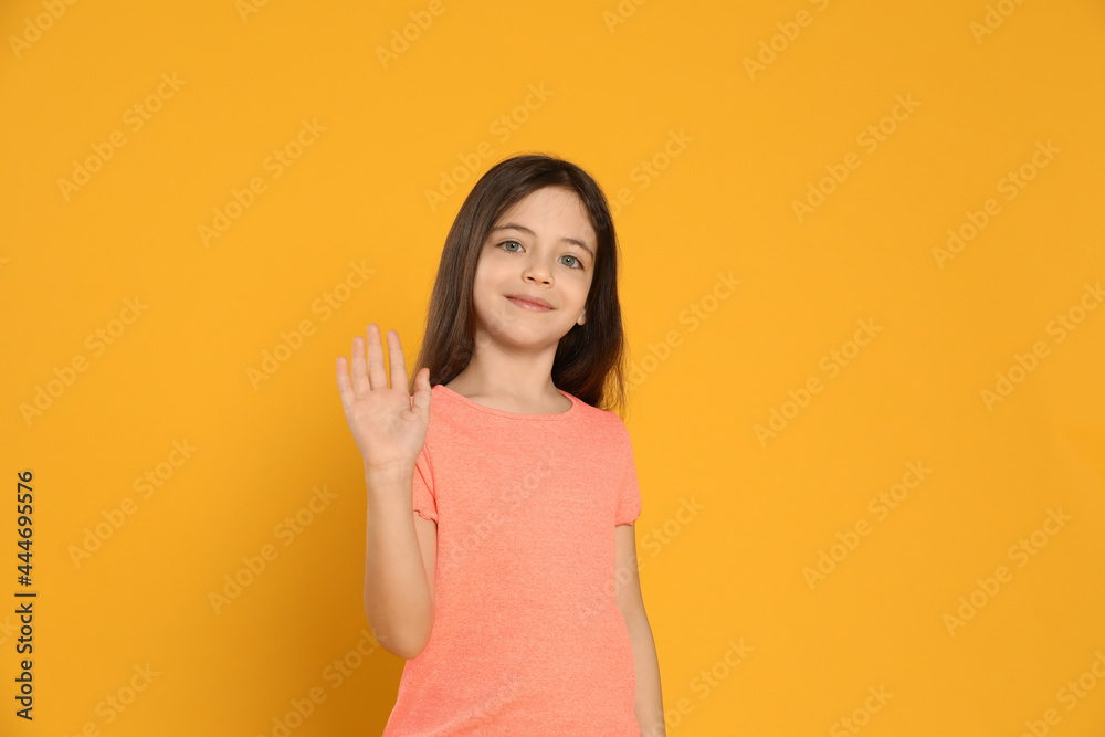 Happy little girl waving to say hello on yellow background