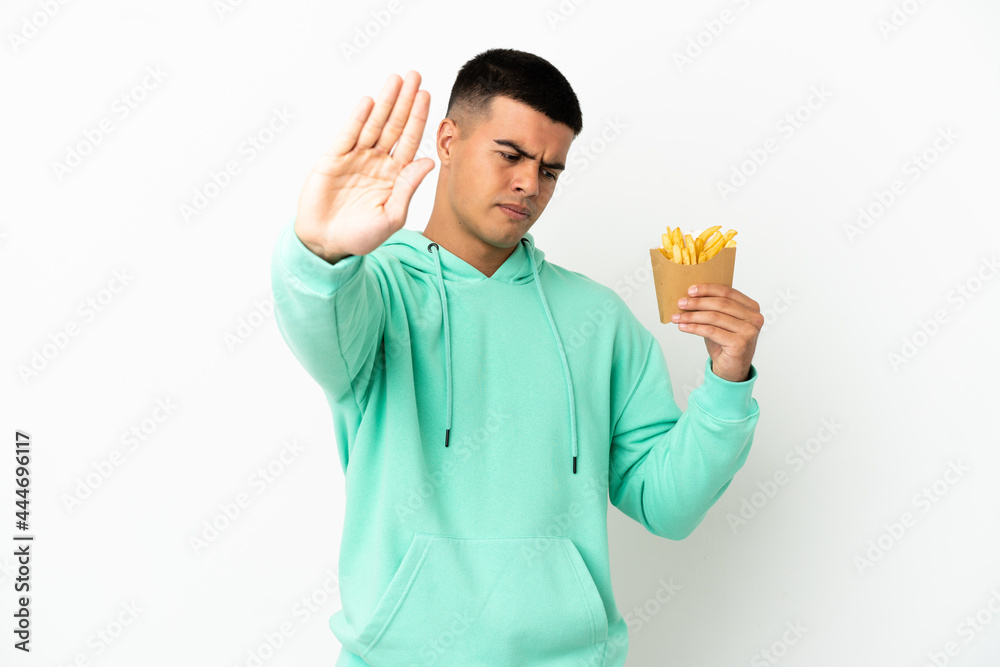 Young handsome man holding fried chips over isolated white background making stop gesture and disappointed Young handsome man holding fried chips over isolated white background making stop gesture and disappointed