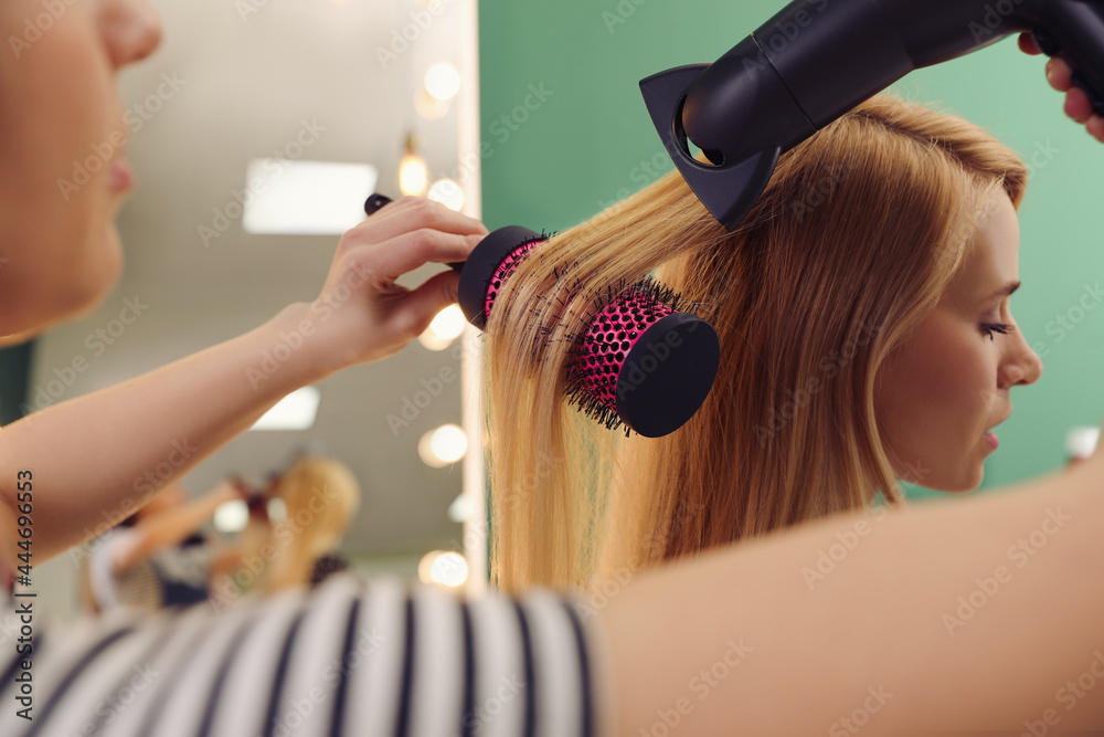 Stylist blow drying woman's hair in salon - obrazy, fototapety, plakaty 