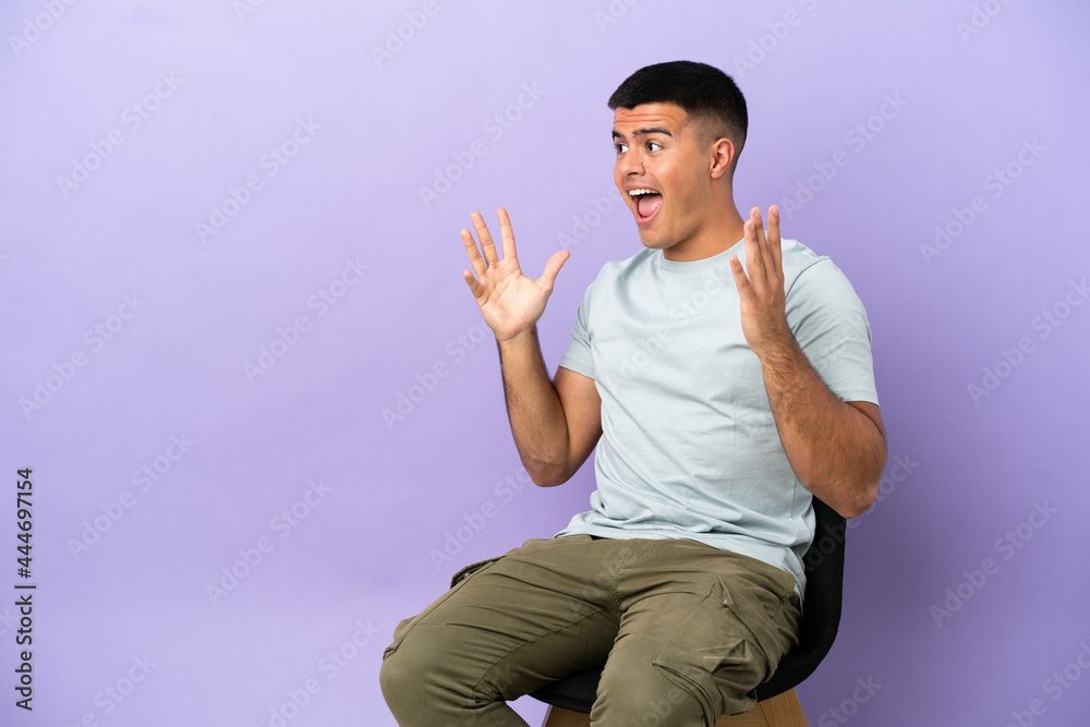 Naklejka premium Young man sitting on a chair over isolated background with surprise facial expression