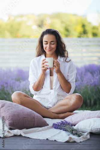 Young woman with long curly hair relaxing with a cup of tea on porch with beautiful view on a lavender field.