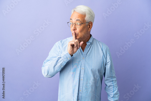 Middle age Brazilian man isolated on purple background showing a sign of silence gesture putting finger in mouth © luismolinero