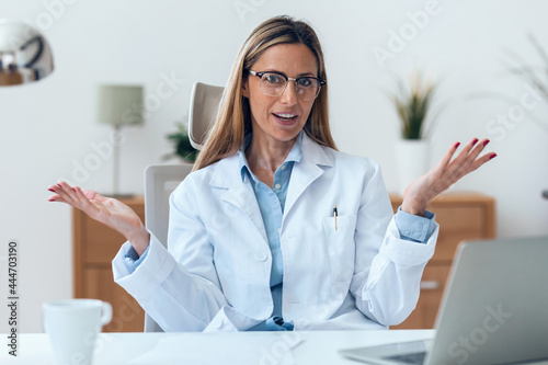 Mature attractive female doctor looking at camera while working sitting in the consultation.