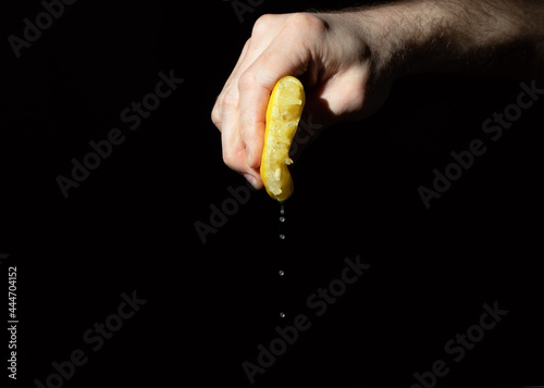 lemon with leaking juice squeezed in hand of man on black background. squeezed like lemon