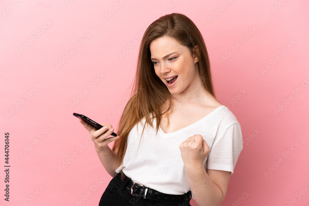 Teenager girl over isolated pink background using mobile phone and doing victory gesture Teenager girl over isolated pink background using mobile phone and doing victory gesture