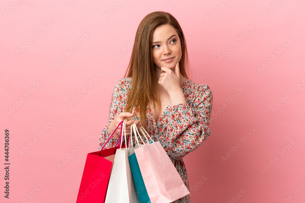 Teenager girl over isolated pink background holding shopping bags and thinking