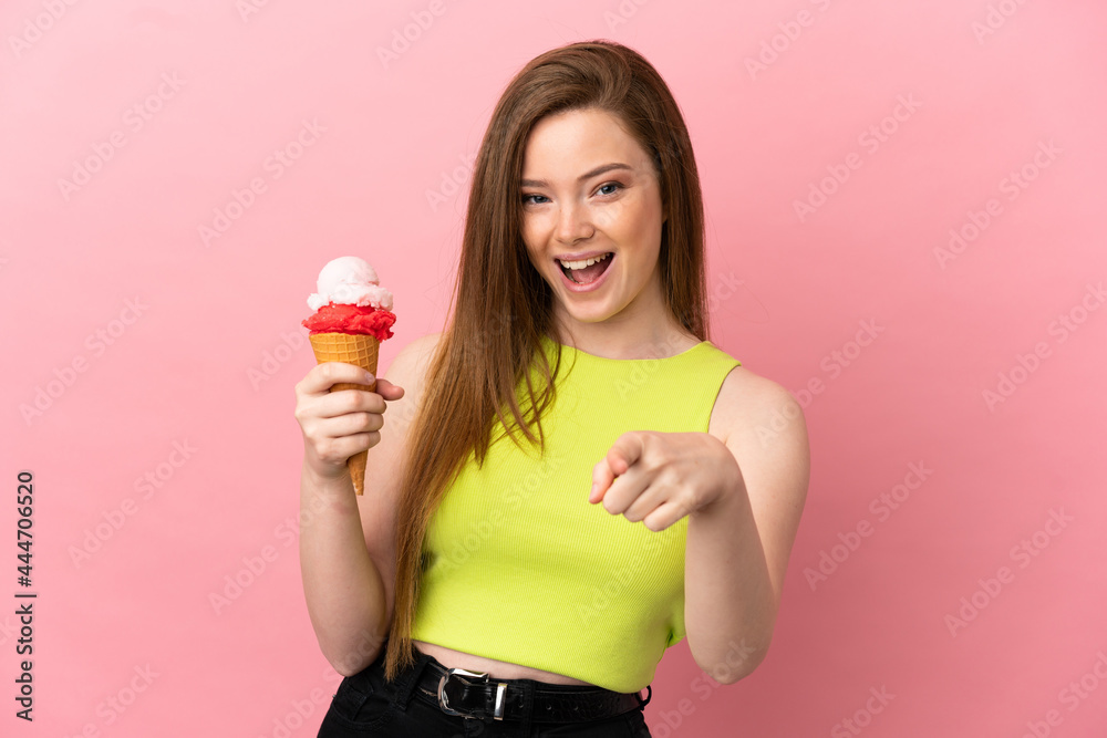 Teenager girl with a cornet ice cream over isolated pink background surprised and pointing front Teenager girl with a cornet ice cream over isolated pink background surprised and pointing front