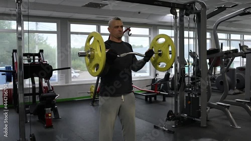 A man in sportswear, with tattoos, with partially shaved hair, does a barbell press with his hands. Exercises for biceps.