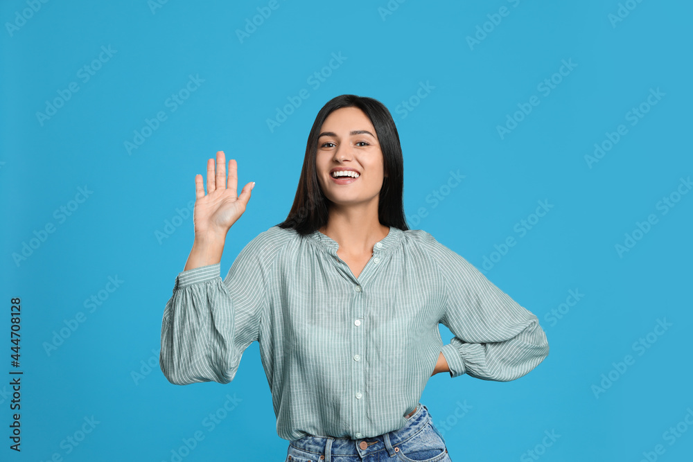 Happy woman waving to say hello on light blue background Happy woman waving to say hello on light blue background