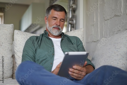 Obraz na plátně Mature handsome man websurfing on tablet at home.