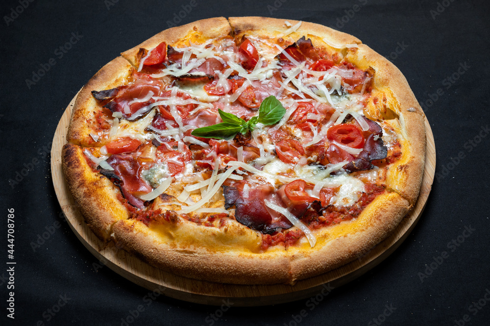 Pizza with tomato sauce, smoked pork ham, chery tomatoes and gorgonzola cheese on a black background