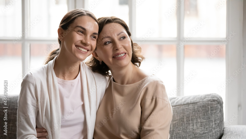 Smiling mature Caucasian 60s mother and adult millennial daughter relax at home look in distance dreaming planning. Happy middle-aged mom and grownup child rest together on family weekend. Smiling mature Caucasian 60s mother and adult millennial daughter relax at home look in distance dreaming planning. Happy middle-aged mom and grownup child rest together on family weekend.
