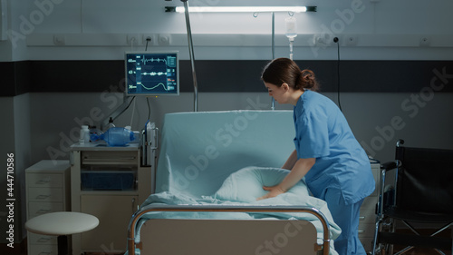 Medical nurse organizing blanket and pillow on hospital bed in clinical ward for treatment. Emergency room designed for recovery patients, surgery, illness, disease healthcare help