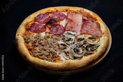 Pizza with tomato sauce  salami  smoked ham  ground tuna and mushrooms on a black background.