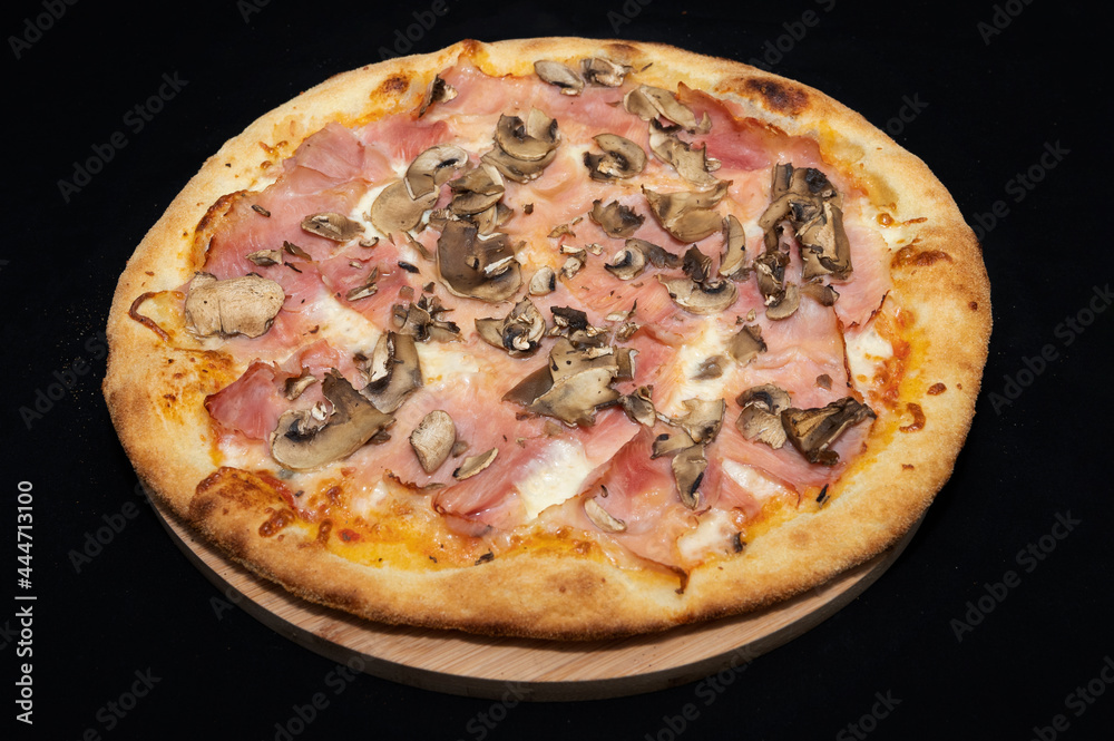 Pizza with tomato sauce, mozzarella, smoked pork ham and mushrooms on a black background.