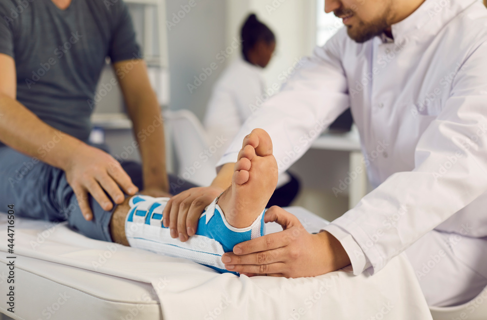 Man's leg in a bandage. Close up of a traumatologist providing medical care to a patient with sprained ligaments in his leg. Concept of treatment of serious physical injuries. Selective focus. Man's leg in a bandage. Close up of a traumatologist providing medical care to a patient with sprained ligaments in his leg. Concept of treatment of serious physical injuries. Selective focus.