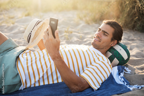 Handsome guy chilling at the beach. Young man using the phone while resting on the sandy beach. photo