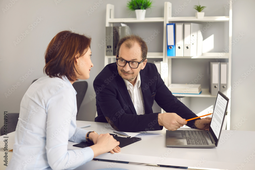 Portrait of two colleagues working together in office. Mature businessman presenting using laptop explaining business idea to female partner. Broker agent showing insurance offer advantage to client Portrait of two colleagues working together in office. Mature businessman presenting using laptop explaining business idea to female partner. Broker agent showing insurance offer advantage to client