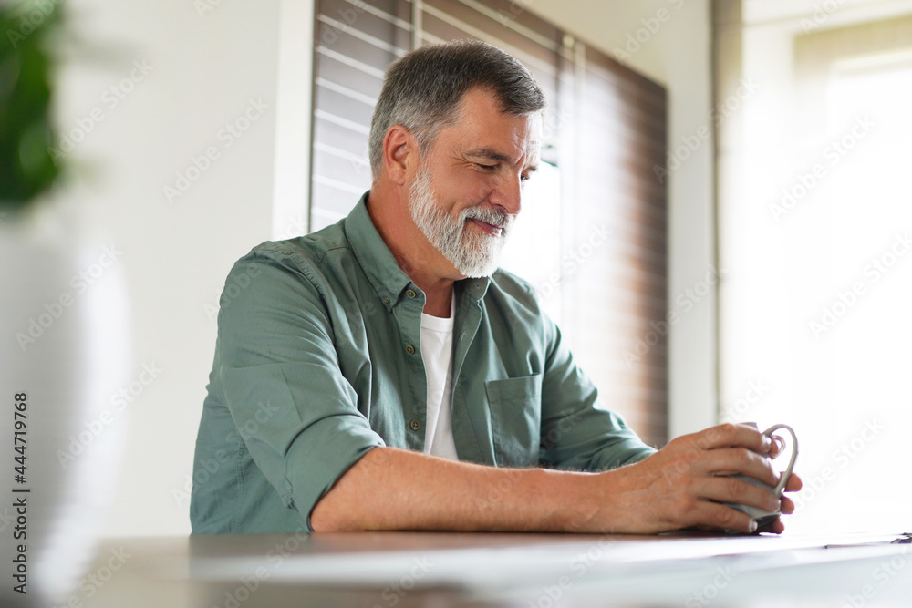 Happy mature man drinking coffee at home in the kitchen, enjoying hot drink in the morning on weekend Happy mature man drinking coffee at home in the kitchen, enjoying hot drink in the morning on weekend