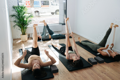 Dedicated group practicing yoga in front of an instructor, raising straight leg up, with strap assistance, while lying on the floor. photo