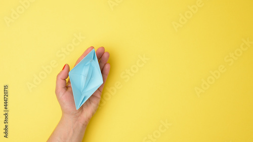 female hand hold a blue paper boat on a yellow background. Mentoring and support concept