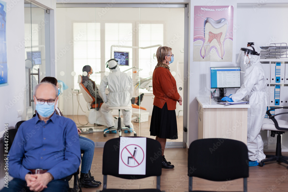 Obraz premium Dentist doctor in ppe suit consulting patient in dental clinic dressed in ppe suit as safety precation during global pandemic with coronaivurs. Senior woman talking with dentistiry stomatology