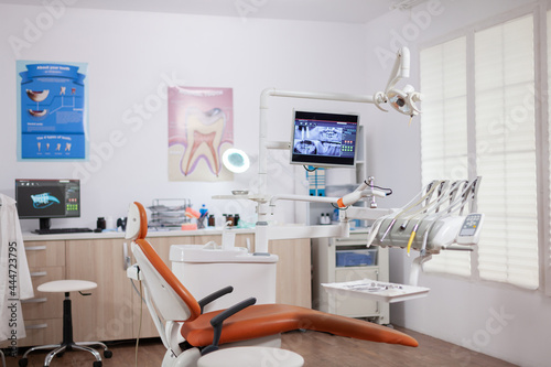 Interior of empty operating room in dental clinic. Stomatology cabinet with nobody in it and orange equipment for oral treatment. © DC Studio