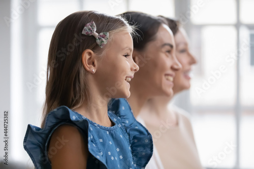 Close up side view of smiling three generations of Caucasian woman look in distance dream of future. Happy little girl with mother and grandmother show young old family line. Unity, bonding concept. photo