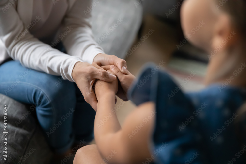 Crop close up of loving young mother hold small teen daughter hands show love and care in relations. Attentive mom caress comfort support little girl child. Family unity, motherhood concept.