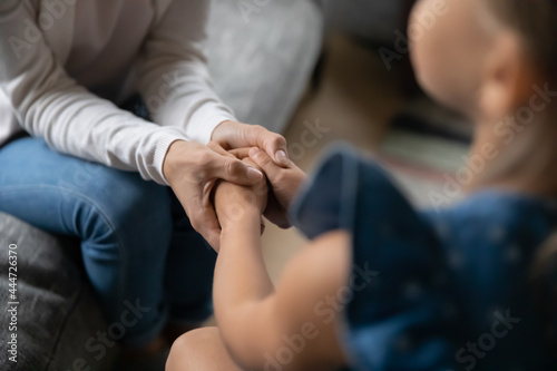 Crop close up of loving young mother hold small teen daughter hands show love and care in relations. Attentive mom caress comfort support little girl child. Family unity, motherhood concept.