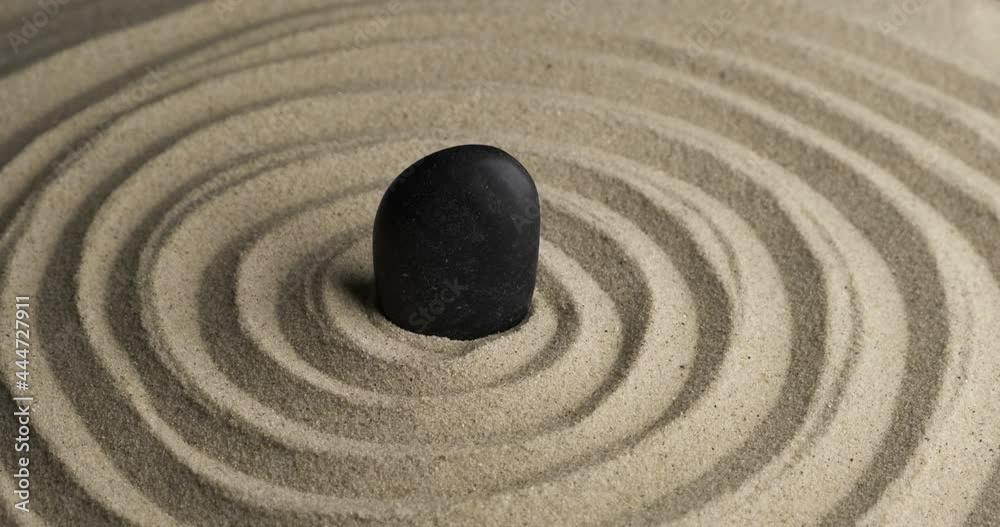 Rotation of the black stone in the center of the sand spiral. Close-up of patterns in the sand. Sand texture