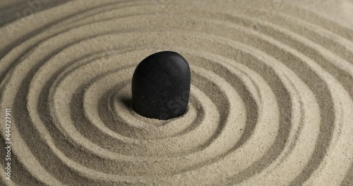 Rotation of the black stone in the center of the sand spiral. Close-up of patterns in the sand. Sand texture