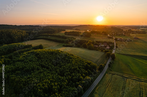 Aerial drone view of golden summer sunset in rural countryside with fields and forest