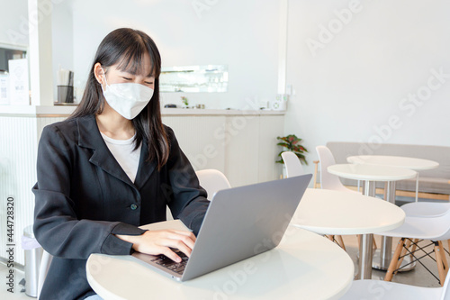 Asian woman wear mask and using laptop in coffee shop.