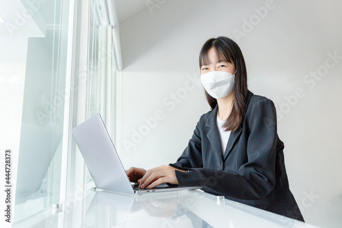 Asian woman wear mask and using laptop in coffee shop.