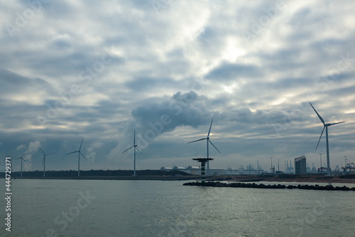 Wind farms onshore along a water channel in the Netherlands. Wind turbines by the water on the shore.