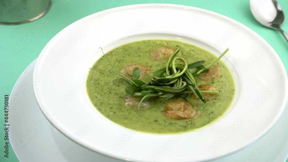 Zucchini and shrimp cream soup. A healthy green lunch. Summer food. Vegetable soup in a white plate. Portion at the restaurant on the table.  Top view