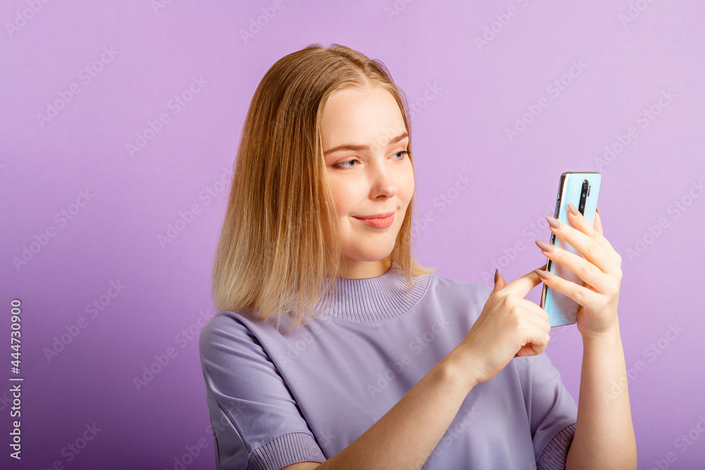Young woman use smartphone sending message via app holding phone over isolated color purple background.